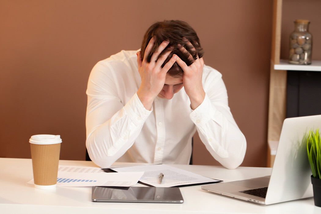 Man zit gefrustreerd achter zijn bureau op het werk als beeld van stress, prestatiedruk en beginnende burn-out waarvoor wandelcoaching kan helpen in Rotterdam, Vlaardingen en Zoetermeer.